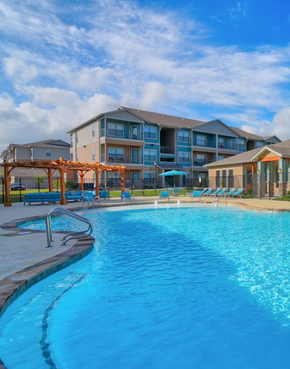 A large swimming pool in front of a building with lounge chairs around it.