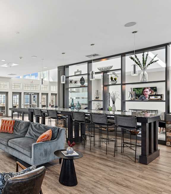 A residential lounge area with a grey couch, an island countertop, and barstool chairs at Parkstone at Knightdale apartments in Knightdale, NC. 