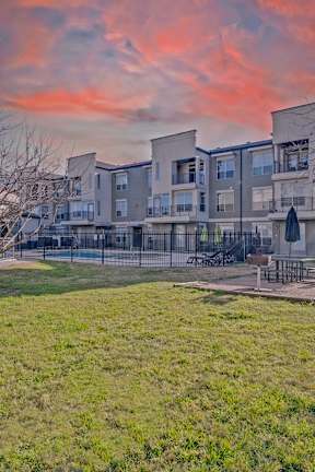 A sunset view of apartment buildings with a green lawn in the foreground. at Millennium on Post Apartments, Texas