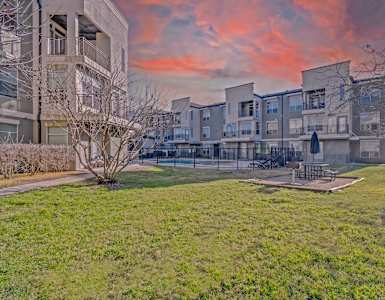 A sunset view of apartment buildings with a green lawn in the foreground. at Millennium on Post Apartments, Texas