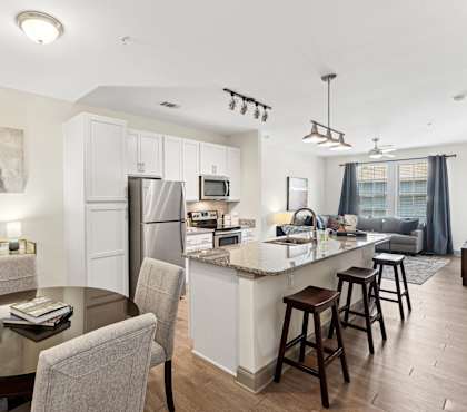 An interior view of a kitchen with a kitchen island countertop and a dining area with a dining table and chairs at Parkstone at Knightdale apartments in Knightdale, NC.