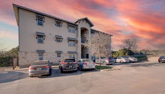 A parking lot with cars and a building in the background. at Logan Ridge Apartments, San Marcos, 78666