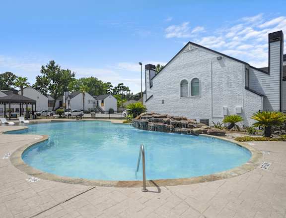 A large outdoor swimming pool surrounded by a patio and a white building.