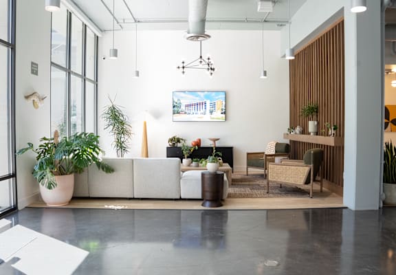A modern office lobby with a large white sofa, a wooden side table, and a TV mounted on the wall.