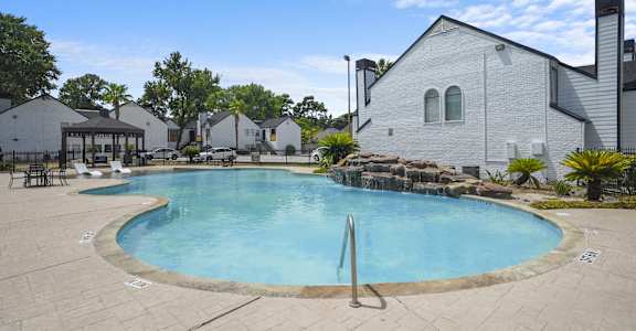 A large outdoor swimming pool surrounded by a patio and a white building.