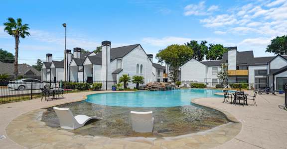 A pool surrounded by a stone patio and chairs.