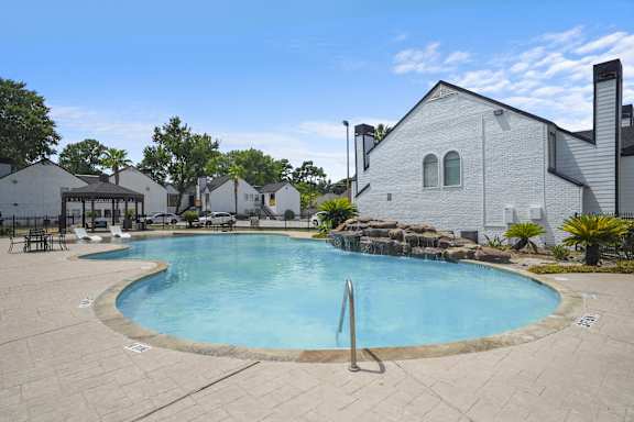 A large outdoor swimming pool surrounded by a patio and a white building.
