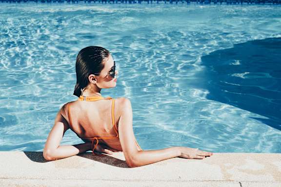 A woman in a yellow bikini is sitting by a pool.