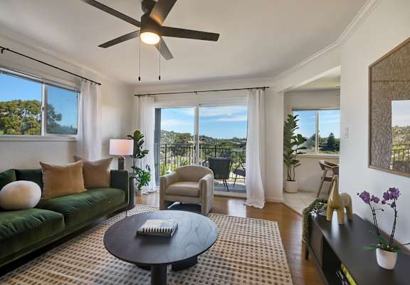 A living room with a green couch, a coffee table, and a ceiling fan.