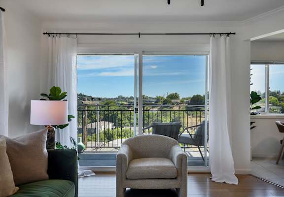 A living room with a green couch, a chair, and a view of the outside through a sliding glass door.