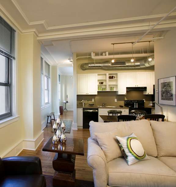 A living room with a sofa, a coffee table, a painting, a ceiling fan, and a bedroom in the background.