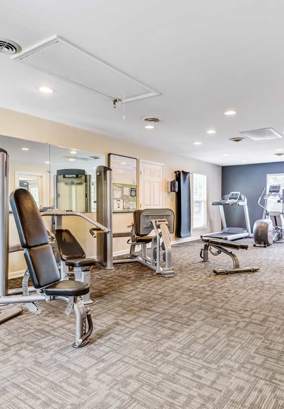 A gym with a variety of equipment including a bench press, a squat rack, and a mirror.