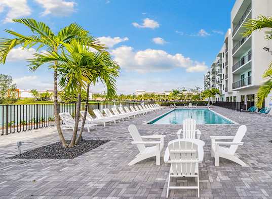 a pool with chairs and palm trees next to a building