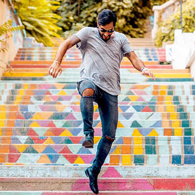 A man in a grey shirt and black jeans is dancing on a colorful staircase.