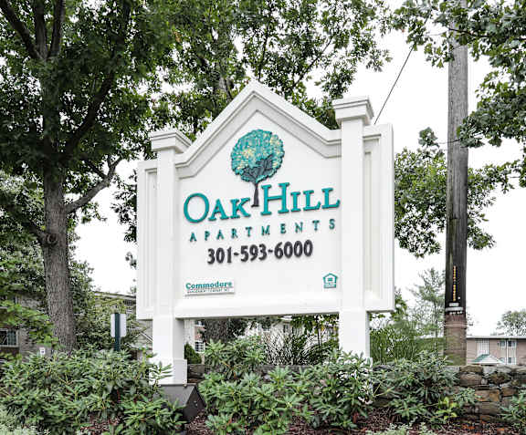 A sign for Oak Hill Apartments is displayed in front of a tree.
