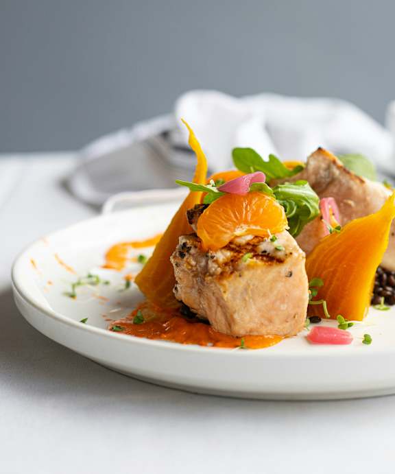 A white plate with a piece of meat and orange slices on it.