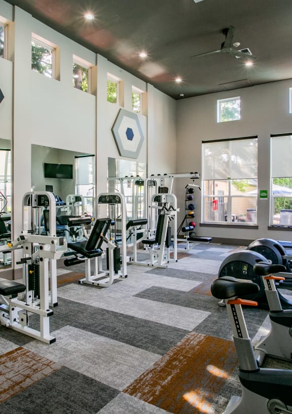 a gym with cardio equipment and windows at the district at highland village apartments