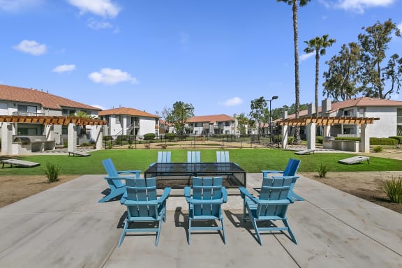a patio with a table and chairs and a grassy area with palm trees in the background
