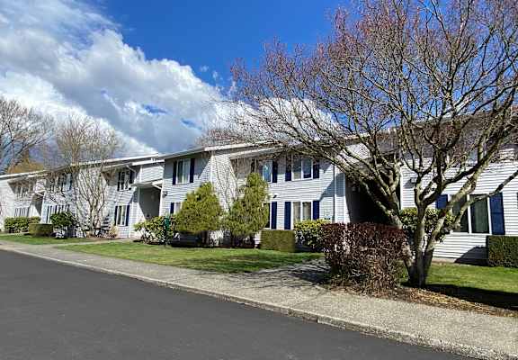Apartments with grass yards in front, landscaping, trees and a paved walkway. Blue skies are behind the apartments.at The Trail, Snohomish, WA 98290