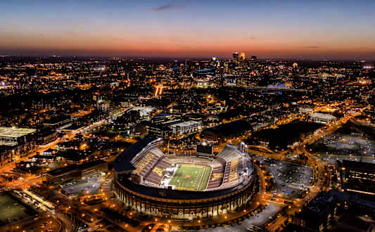 A stadium is lit up at night with a city in the background.