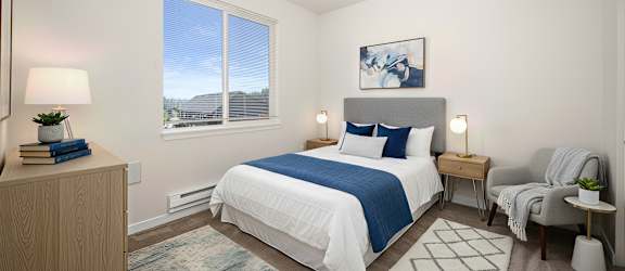 A bedroom with a large bed, a nightstand, a chair, and a window with a view of the outside.