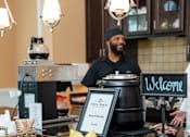 Thumbnail 3 of 17 - A man is standing behind a counter with a sign that says "Welcome".