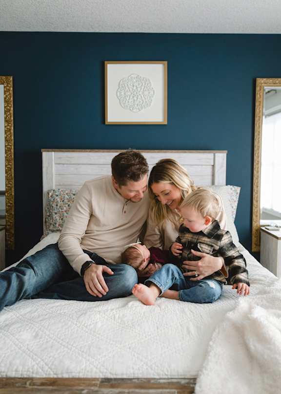 A family of three is sitting on a bed together.