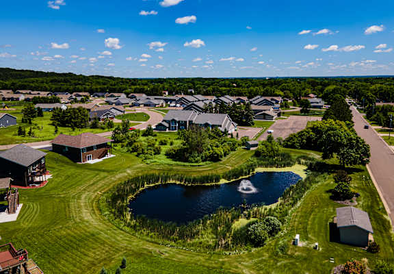 A bird's eye view of a residential area with houses and a pond.