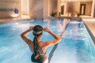A woman is sitting in a pool with her hands behind her head.