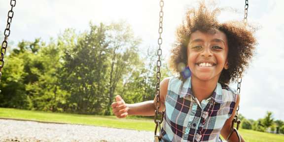 A girl is sitting on a swing in a park.