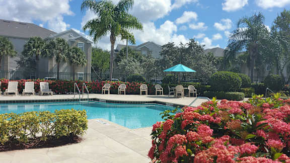 A pool surrounded by chairs and a fence with a house in the background.