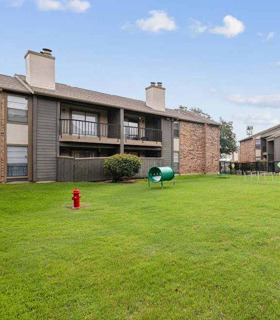 A grassy area in front of apartment buildings with a red fire hydrant and a green lawn chair.