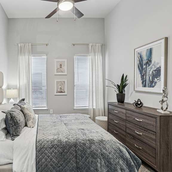 A bedroom with a large bed, a nightstand with a lamp, and a ceiling fan.