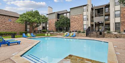 A small pool with a stone border and a few chairs around it.