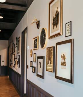 A wall of framed artwork and clocks on a wall.