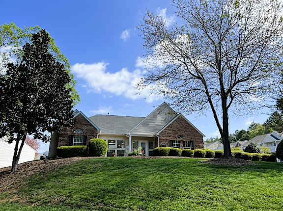 A house with a green lawn and trees in front.