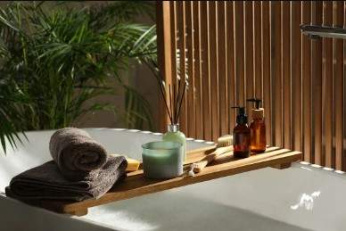 A wooden tray with a candle, towels, and bottles on a white sink.