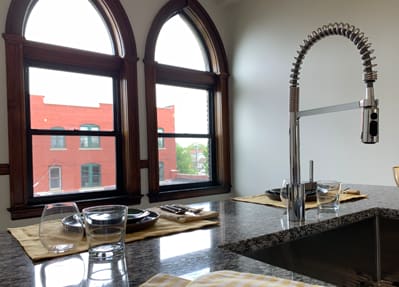 A kitchen with a sink and a window overlooking a red building.