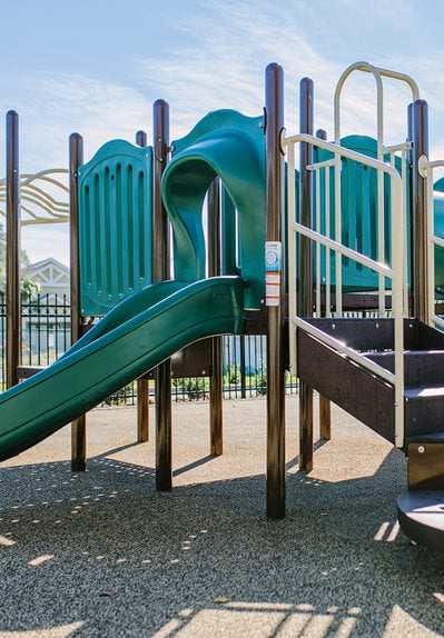 A playground with a green slide and a brown ramp.