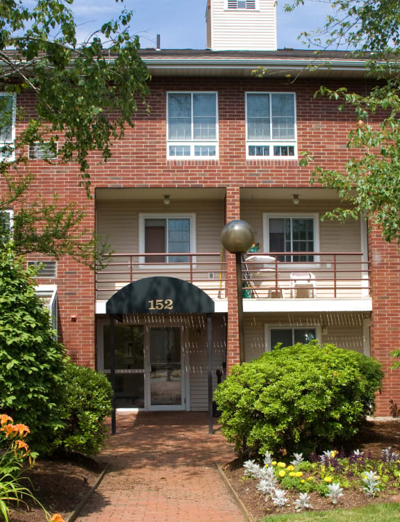 the front of a red brick apartment building with a sidewalk and trees