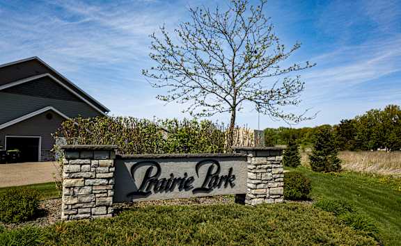 A sign that says Prairie Park in front of a house and a tree.