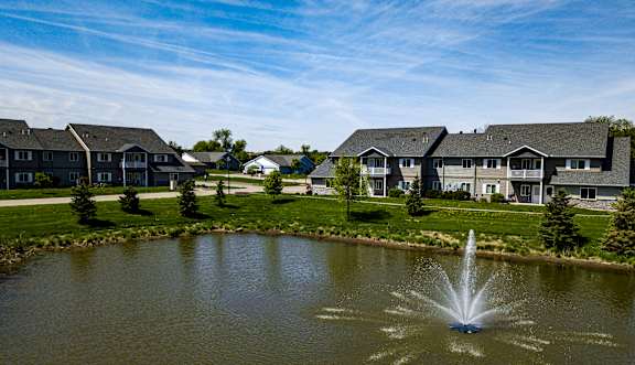 A fountain in the middle of a pond in front of apartment buildings.