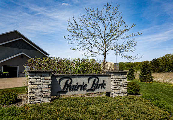 A sign that says Prairie Park in front of a house and a tree.