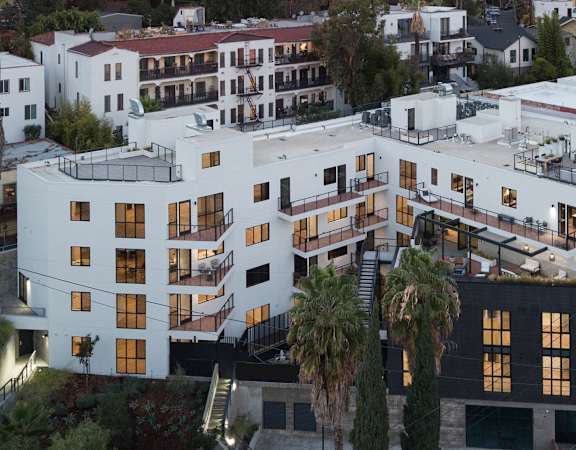 A white building with black windows and balconies is surrounded by trees.