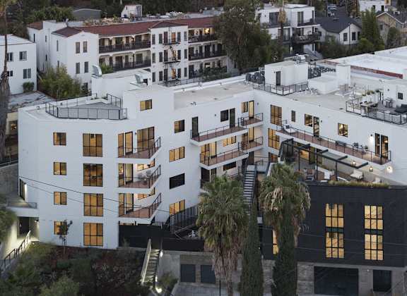 A white building with black windows and balconies is surrounded by trees.