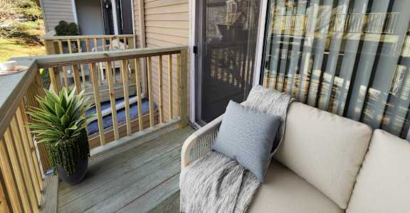 A small balcony with a couch and a potted plant.