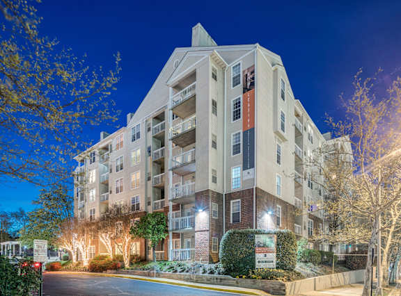 A large apartment building with a lit up entrance and trees in front.