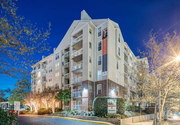 A large apartment building with a lit up entrance and trees in front.
