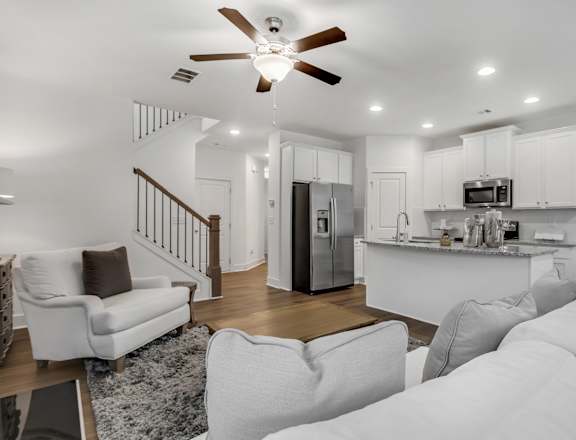 a living room with couches and a kitchen with a staircase
