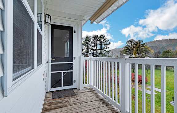 A white door is on a porch with a white railing.